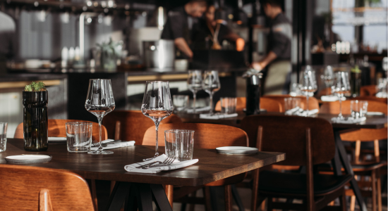 A stylish restaurant setup with neatly arranged tables and glasses, ready for service, with chefs working in the background