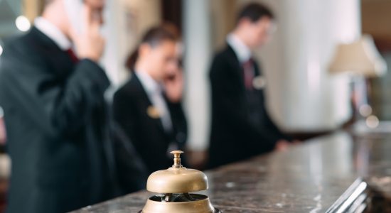 Hotel front desk staff attending to guests over the phone, with a focus on a service bell in the foreground.