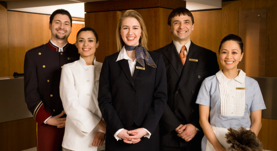 A group of hotel staff, including bellhops, front desk clerks, and housekeeping staff, smiling and standing together.