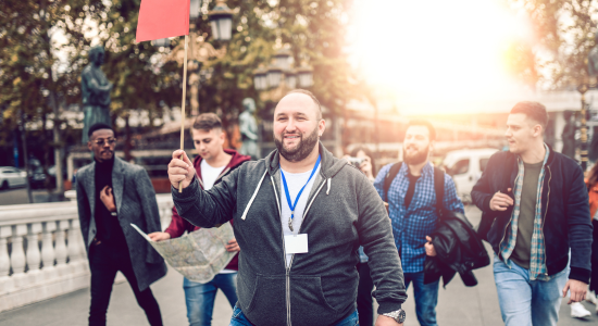 A cheerful tour guide leading a group of tourists on a city tour, holding a red flag and a map.