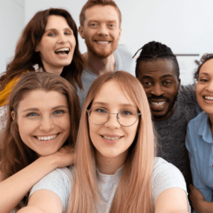 A group of six friends or students huddled together for a selfie. They are all smiling and appear happy, with a mix of men and women of different ethnic backgrounds.