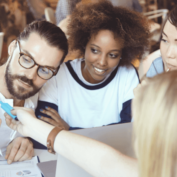 A group of people working together at a table. One person is holding a blue sticky note, and the others are engaged in the discussion, looking at the note and smiling.