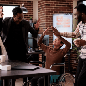 A joyful scene in an office setting where two men are giving high-fives to a young woman in a wheelchair. The atmosphere is celebratory, with smiles and raised hands all around.