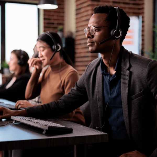 Call center operators wearing headsets are working at their desks in a modern office. They are focused on their tasks, with one person in the foreground and others in the background.