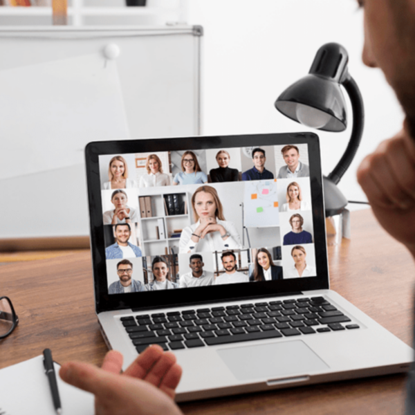 A man participating in a virtual meeting on a laptop, with multiple colleagues visible on the screen.