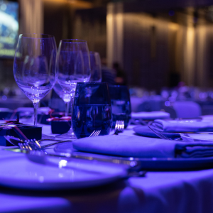 A close-up shot of a formal dining table at the President's Dinner & Training Awards. The table is set with plates, utensils, wine glasses, and water glasses. The table is dimly lit, creating a blue-hued ambiance.