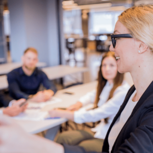 A businesswoman in glasses giving a presentation to a small group of colleagues in a conference room.